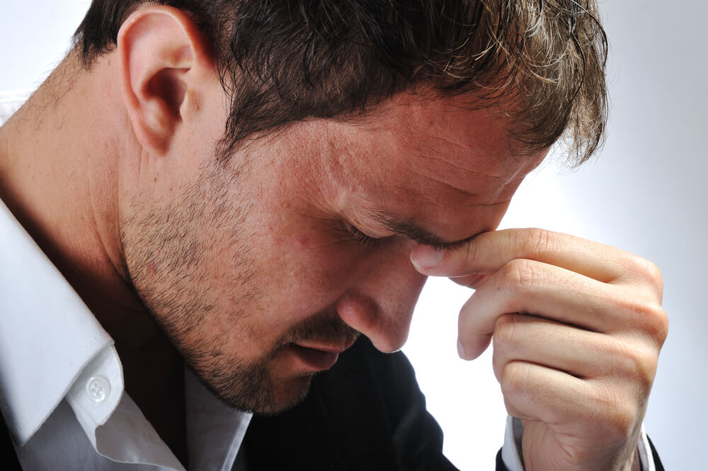 Portrait of a man with a headache pinching his nose.