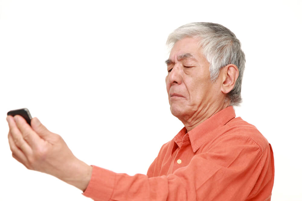 Older man  squinting at phone held arms length out.