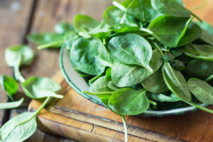 spinach on top of glass plate, on top of a wooden cutting board.