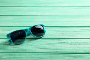 Teal sunglasses against a similarly colored wooden backdrop.