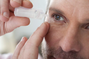 Person applying eye drops to right eye.