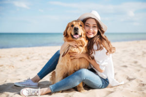 A woman holds a dog against an ocean background. The dog is happy.