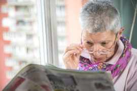 Older woman looking over glasses to read newspaper