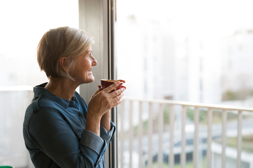 Older woman looking out a window holding a cup of coffee