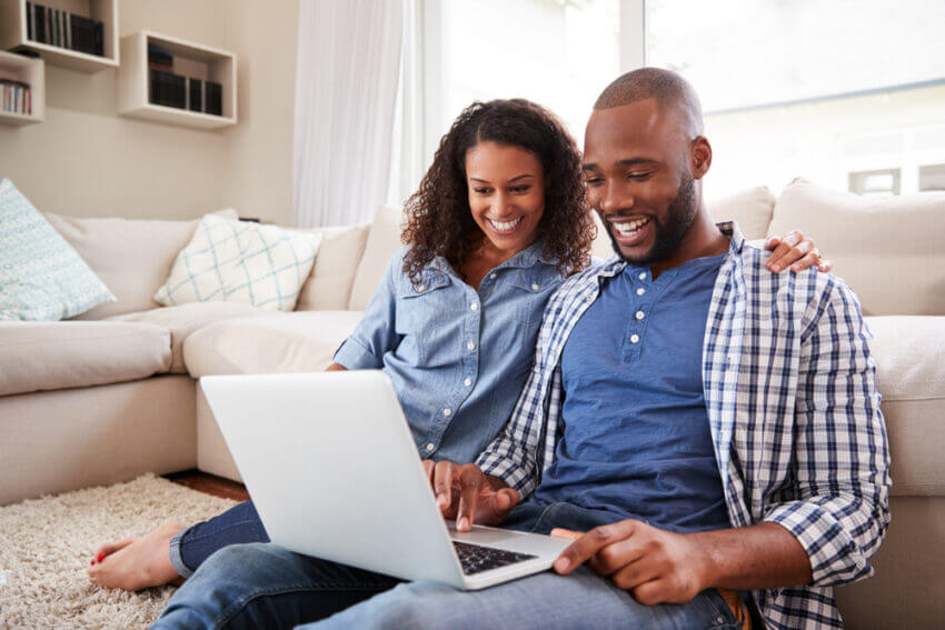 Young couple using laptop sitting on the floor at home